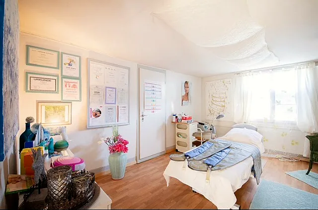 Behandlungsraum mit Liege, Diplomen an der Wand und Blumen